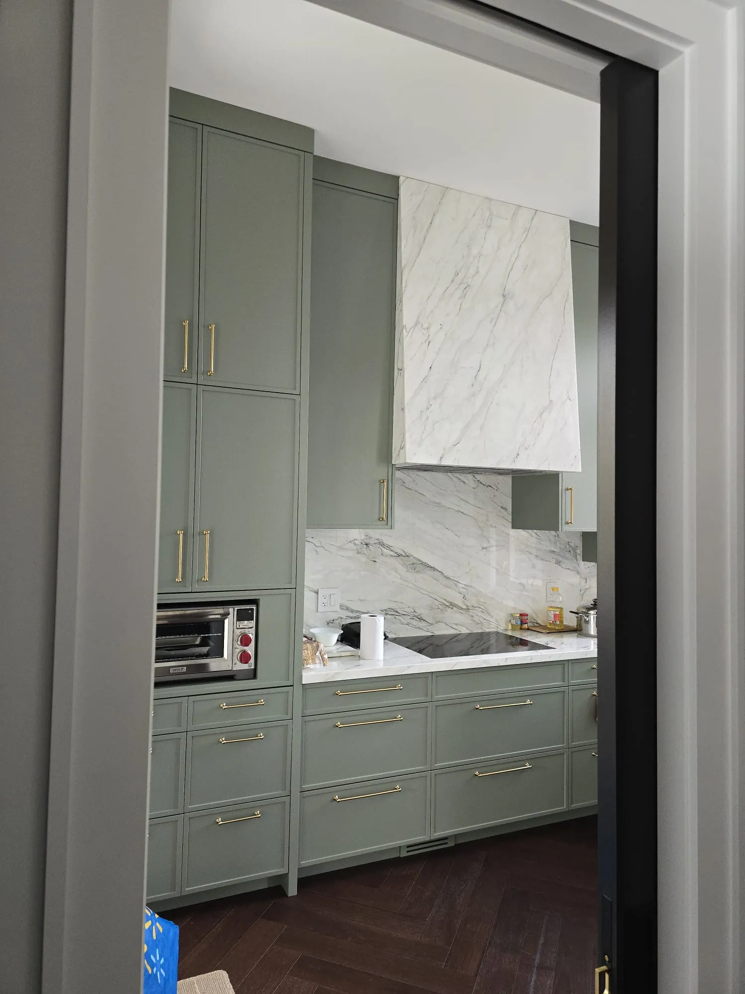 Soft sage-green kitchen cabinets with a marble range hood